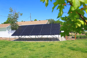 A ground mounted solar array in a grassy backyard with a fence. 
